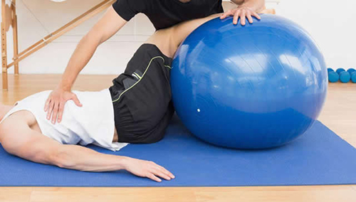 25505637 - physical therapist assisting young man with yoga ball